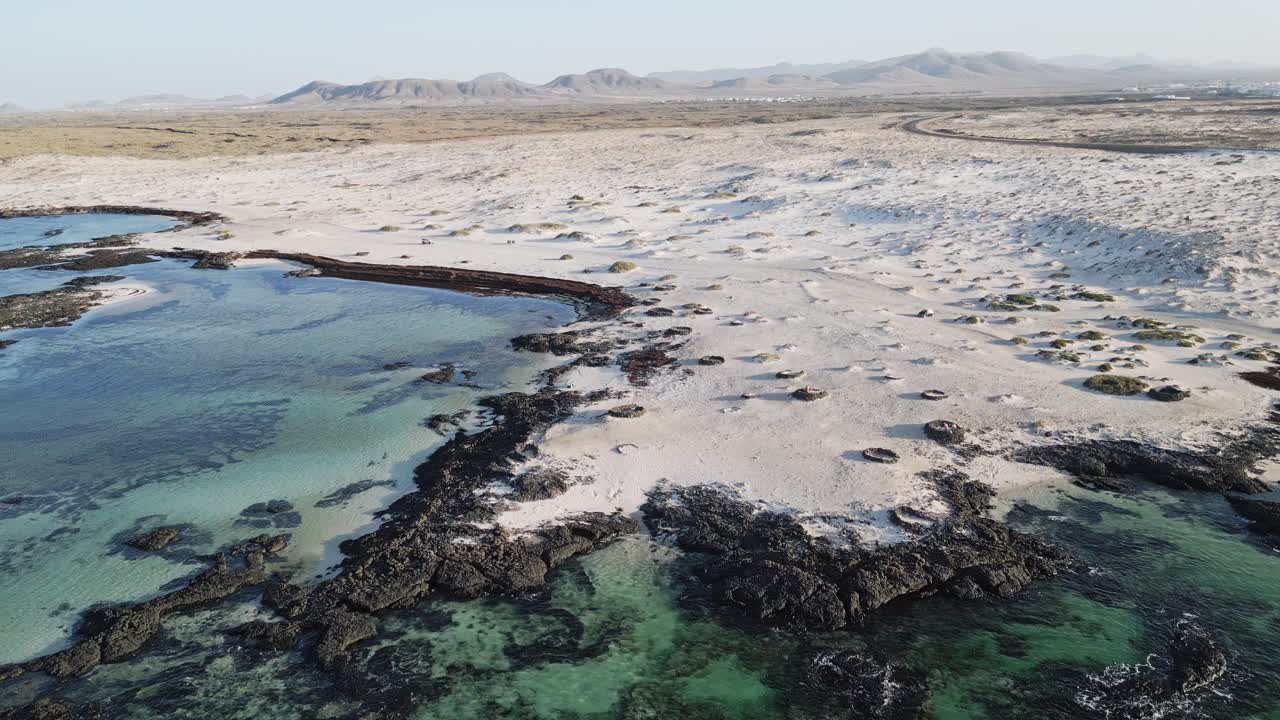Aerial drone shot of a car driving across sandy dunes near El Cotillo, Fuerteventura. Perfect for travel, off-road, and adventure content.