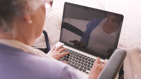 Senior-woman-sitting-on-wheel-chair-using-laptop