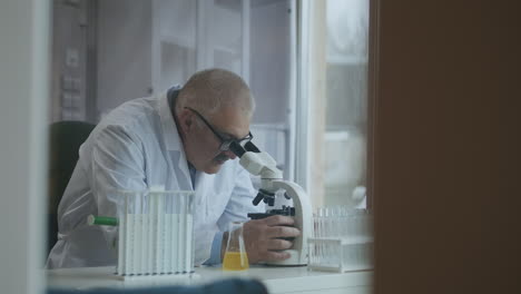 Científico-Investigador-Masculino.-Está-Sentado-En-Un-Laboratorio-Moderno-De-Alta-Gama-Con-Un-Microscopio-De-Cristalería-Y-Monitores-De-Trabajo-A-Su-Alrededor.-Imágenes-4k-De-Alta-Calidad