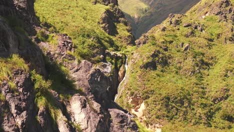 Drone-image-emerging-from-behind-rocks-and-revealing-a-beautiful-waterfall-nestled-in-the-Andes-mountains