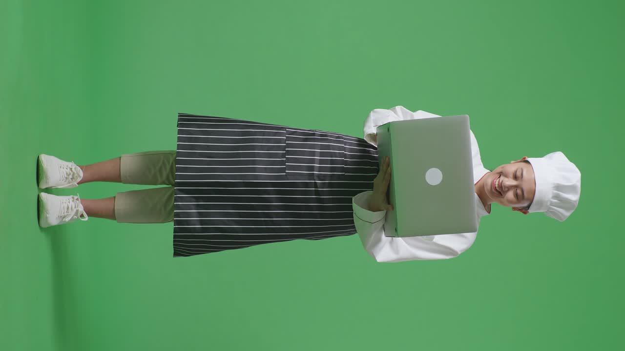 Full Body Of Asian Woman Chef Using A Laptop While Standing In The Green Screen Background Studio