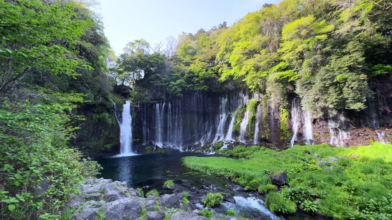 A scenic view of Shiraito Falls near Mount Fuji, showcasing waterfalls, greenery, and clear water