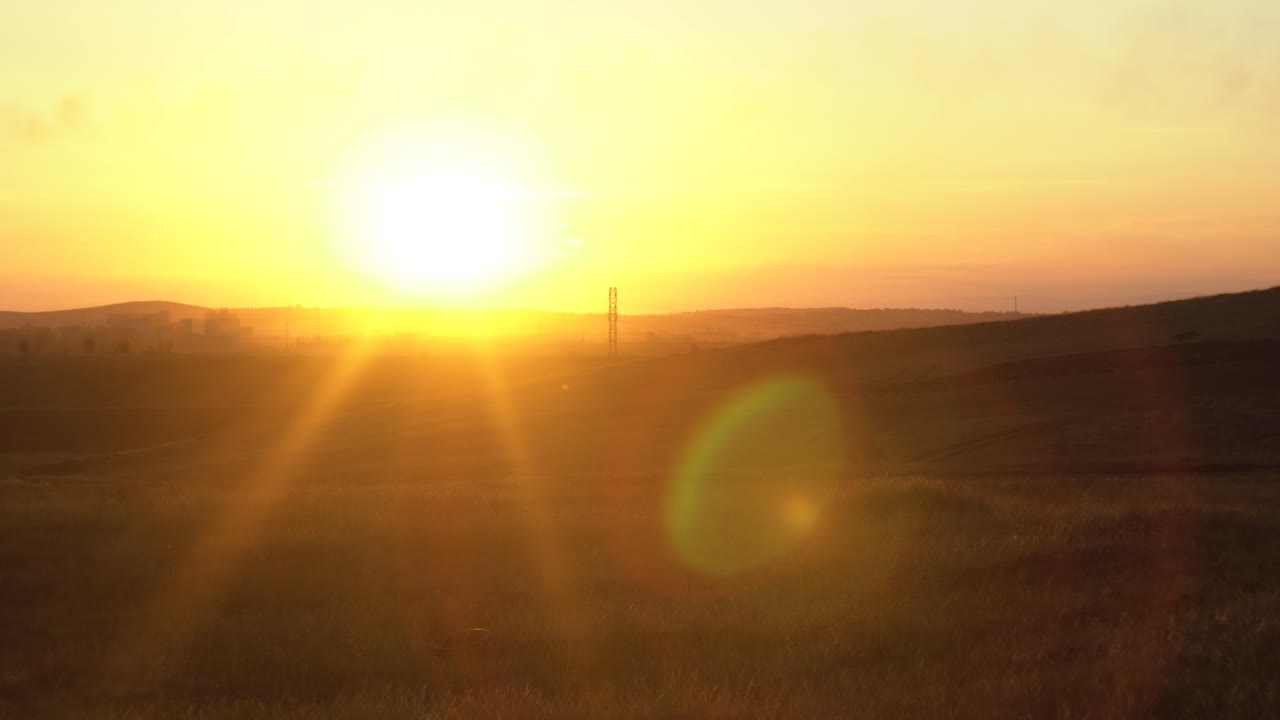 puesta de sol sobre un campo con colinas y estructuras industriales