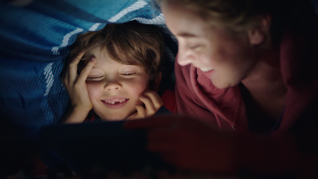 mother and child using tablet computer under blanket playing games on touchscreen technology little boy having fun before bedtime