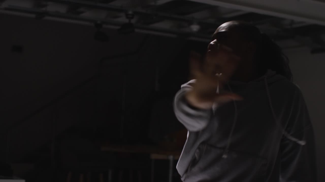 Studio Portrait Shot Of Young Woman Wearing Hoodie Dancing With Low Key Lighting Against Black Background 1