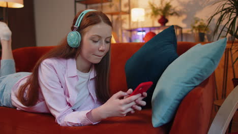 Happy-relaxed-kid-in-wireless-headphones-dancing-listening-favorite-rock-n-roll-music-on-home-couch