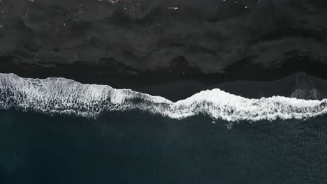 top down slowmotion drone shot of waves rooling on black sand beach in indonesia