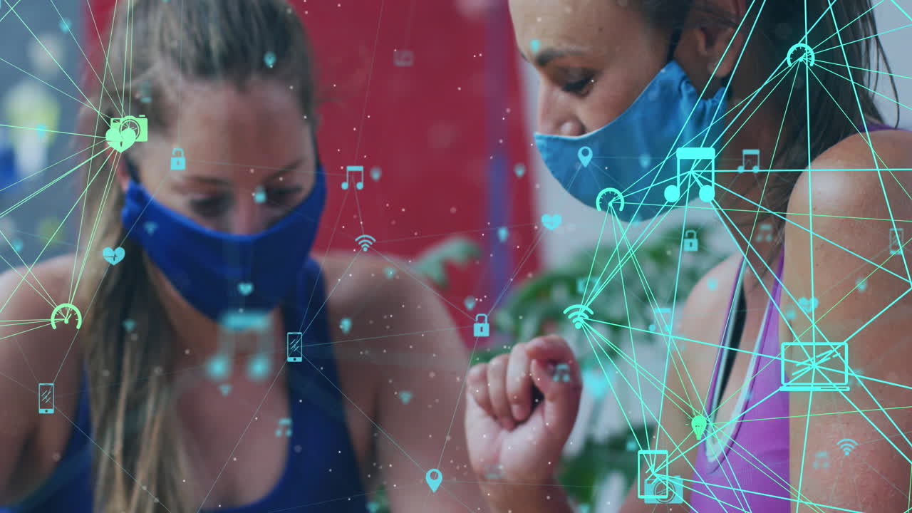 animación de iconos de los medios sobre dos amigas caucásicas con máscaras faciales con teléfonos inteligentes