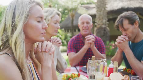 Happy-caucasian-family-having-dinner-and-praying-in-garden