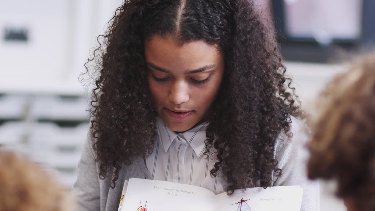primer plano de una joven maestra de escuela preescolar que muestra un libro de imágenes a los niños durante una lección