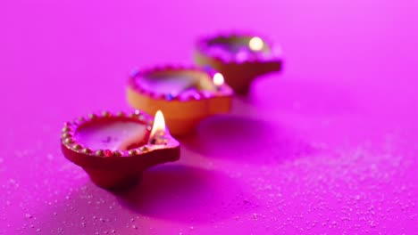 Close-up-of-burning-colourful-candles-celebrating-diwali-on-purple-background