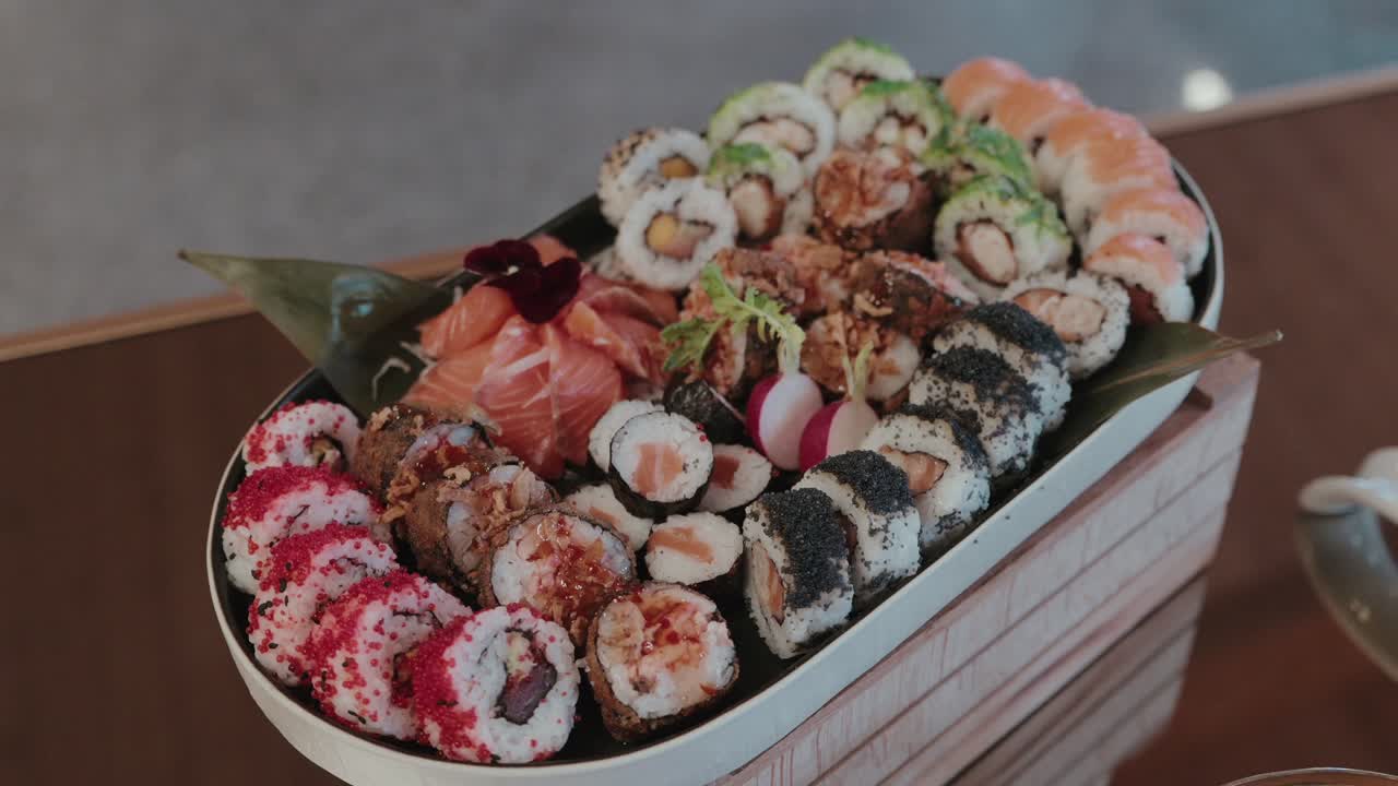 Vista dall'alto di rotoli di sushi assortiti con guarnizioni vivaci e sashimi di salmone su un vassoio elegante.