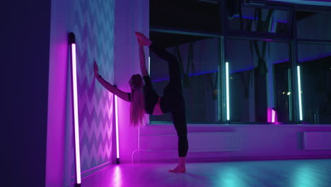 una joven gimnasta se está estirando en el gimnasio apoyándose en la pared y levantando la pierna
