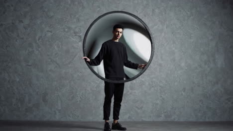 young man posing with a black circular frame in a modern studio