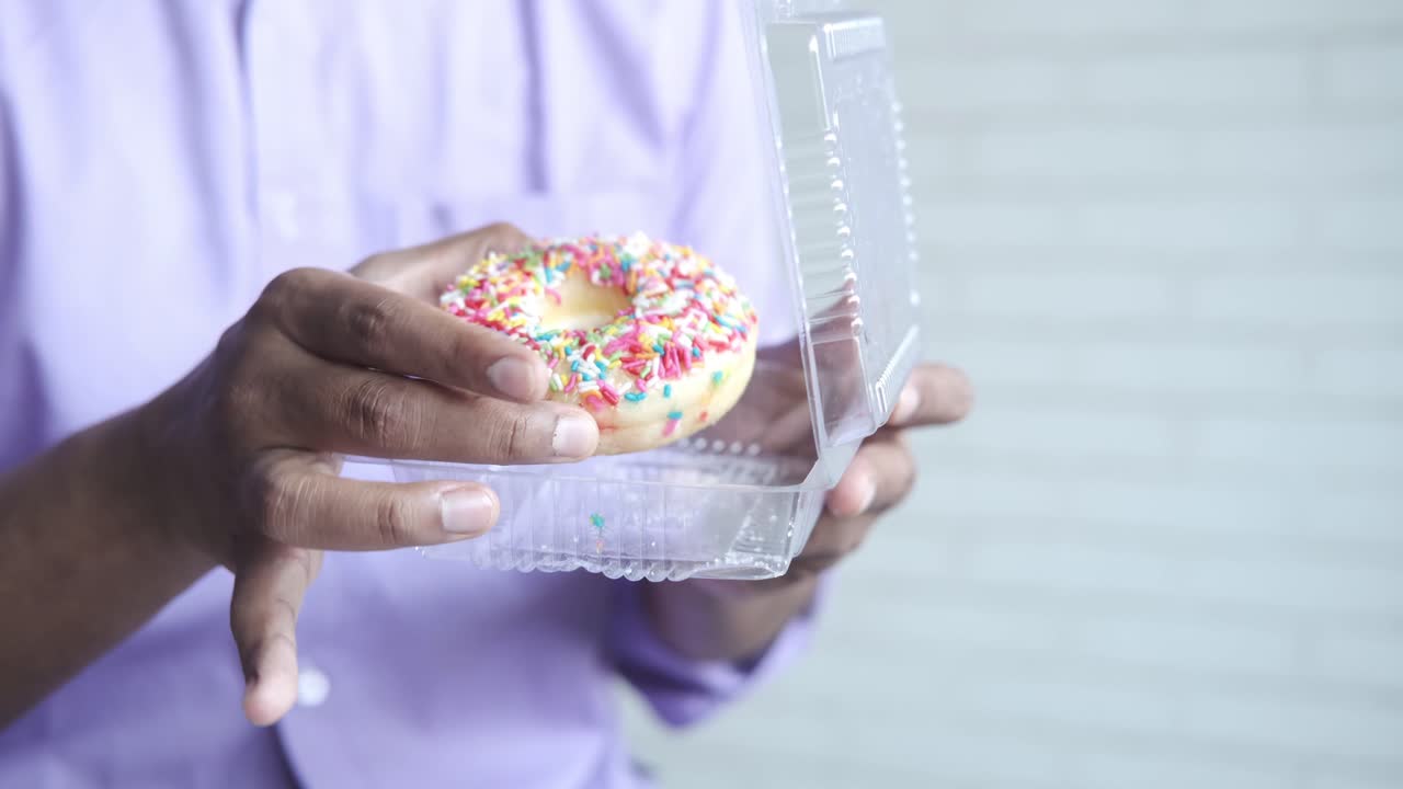 persona sosteniendo una rosquilla en un recipiente de plástico