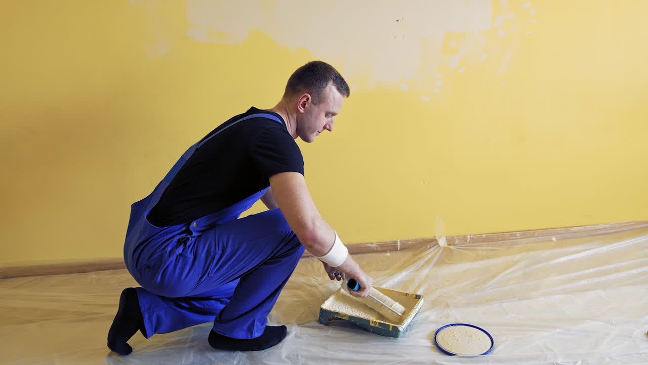 Painter rolling paint roller in color on a tray. Handyman working with a paint roller and having a pain in back. Renovation at home.