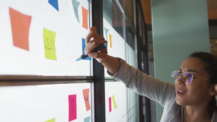 Happy biracial female creative businesswoman writing on memo notes, brainstorming in office