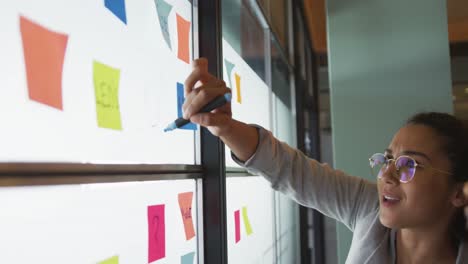 feliz mujer biracial mujer de negocios creativa escribiendo en notas de memoria, lluvia de ideas en la oficina