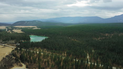 Tree-covered-mountains-with-bright-teal-glacier-lake-under-cloudy-skies