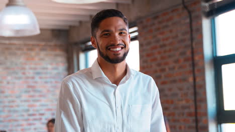 Retrato-De-Un-Hombre-De-Negocios-Sonriente-Parado-En-Una-Oficina-Ocupada-Con-Colegas-Trabajando-En-Segundo-Plano