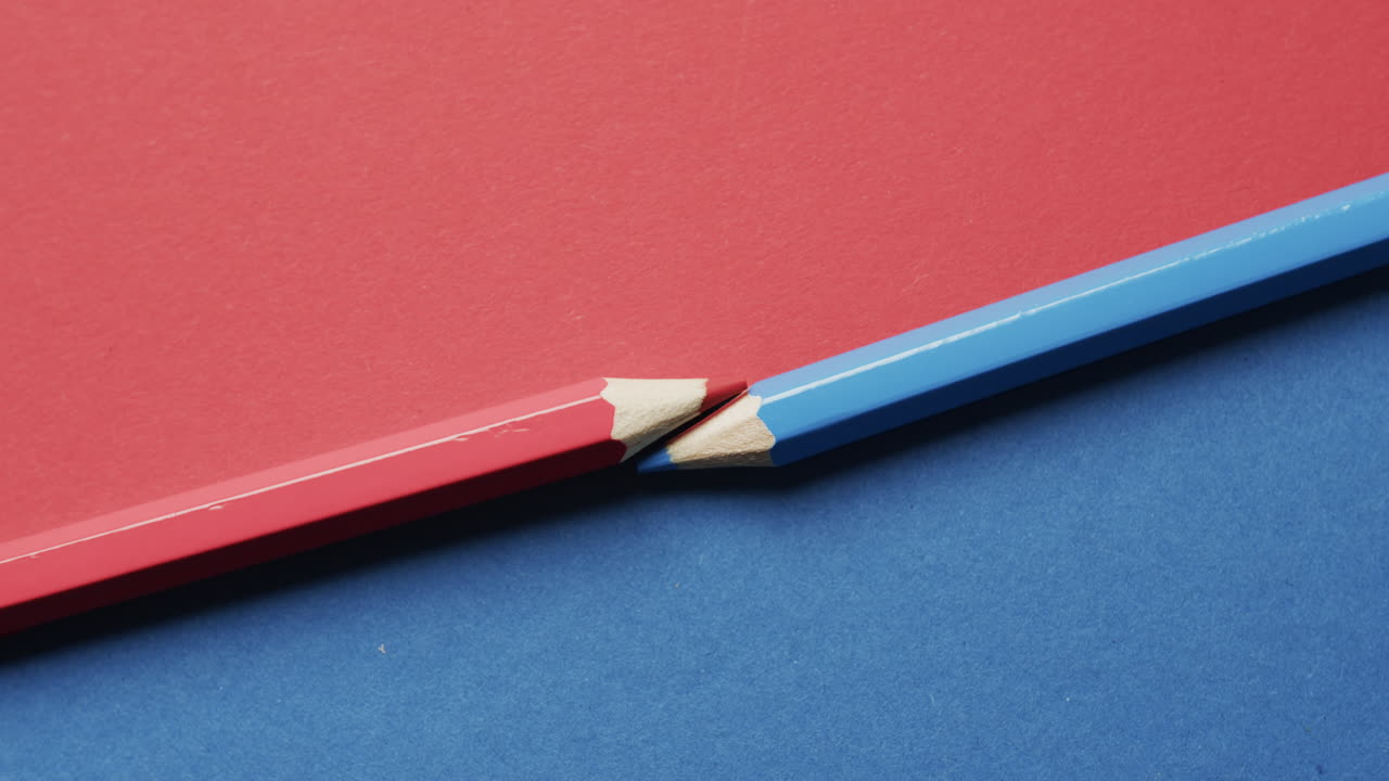 vista aérea de lápices de colores azules y rojos dispuestos sobre fondo rojo y azul, en cámara lenta