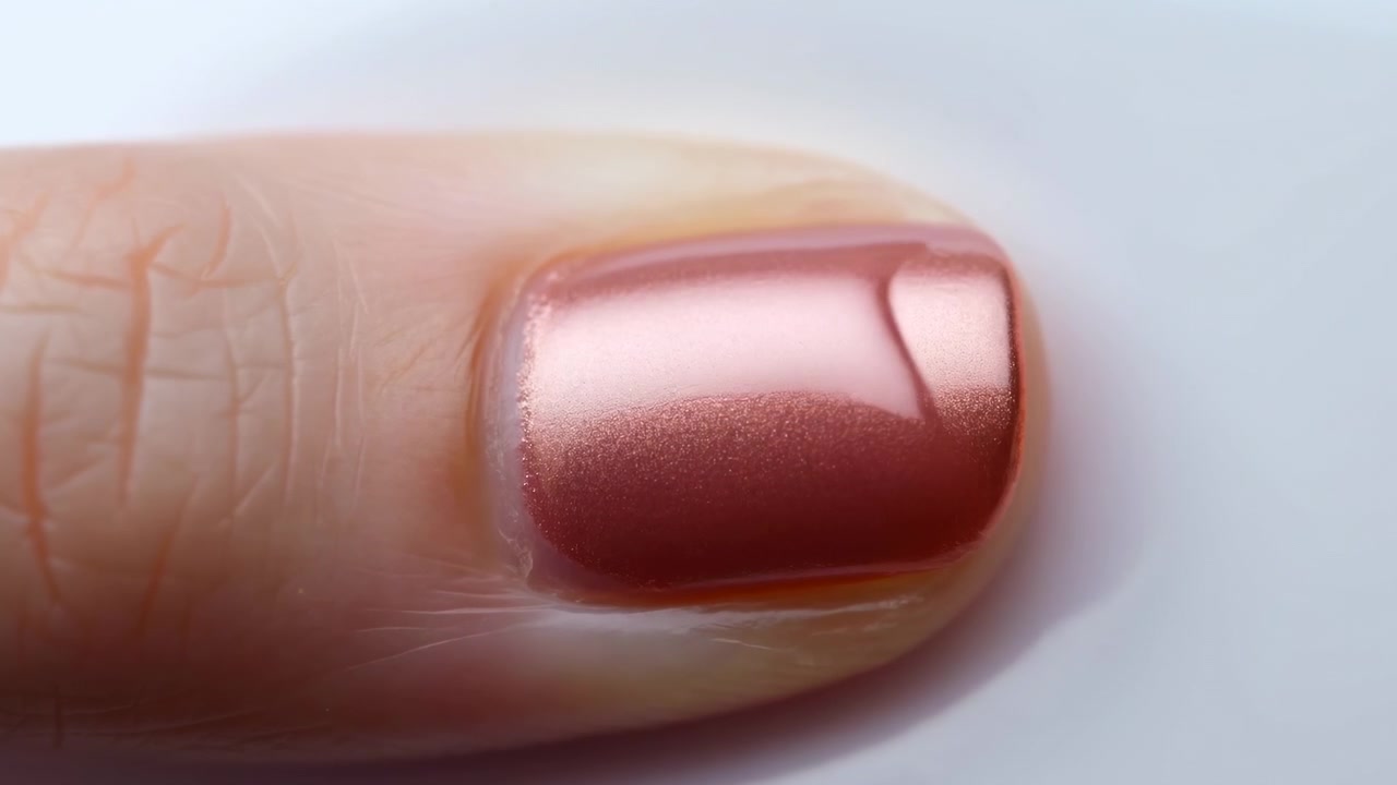 Primo piano di ispezione della manicure dell'unghia del pollice a metà della sequenza di cura che mostra smalto rosa lucido.
