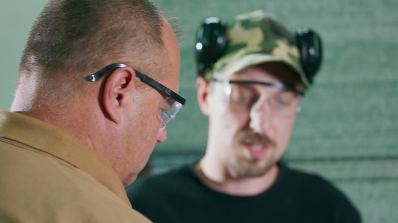 훈련생은 닫힌 사격장에서 강사의 감독하에 총을 기 전에 보호 안경과 이어폰을 착용합니다.