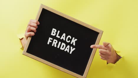 hands holding and pointing at black board with black friday sale text in white, on yellow background