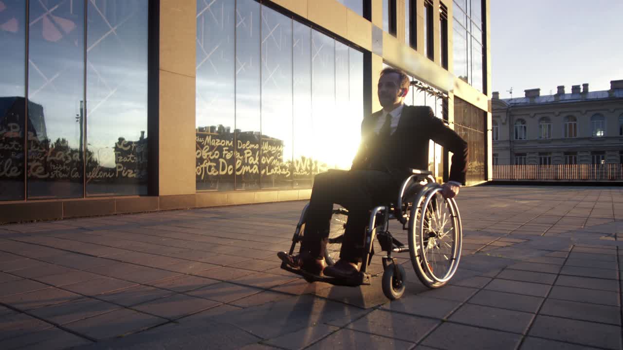 Young attractive entrepreneur business man sitting on wheelchair at sunset outdoor. He in formal suit and tie. Confident and attractive disabled handicapped man.