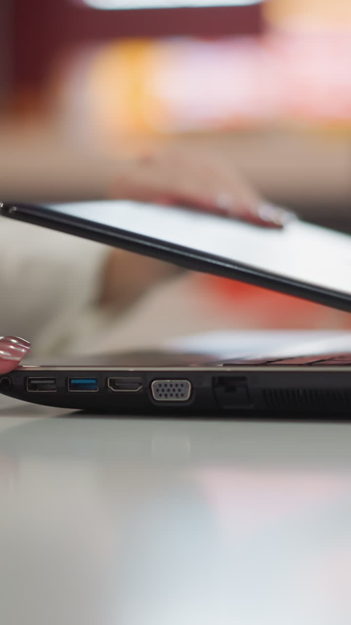 primer plano de manos elegantes con uñas pintadas que alcanzan una computadora portátil cerrada la abre en un entorno interior moderno, el fondo presenta una iluminación suave y borrosa con una sutil luz roja sonora