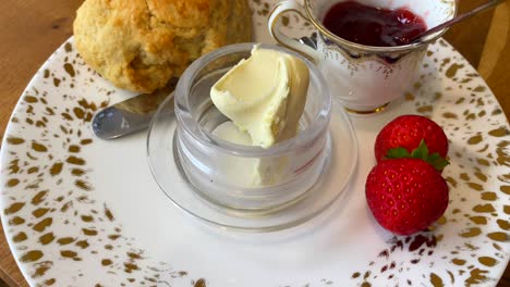 Auténtico-Bollo-Británico-Con-Mermelada-De-Fresa,-Crema-Cuajada-Y-Fresas-Frescas-Con-Una-Taza-De-Té-En-Inglaterra,-Postre-Dulce-Tradicional-Para-El-Desayuno-A-La-Hora-Del-Té-En-El-Reino-Unido,-Toma-De-4k