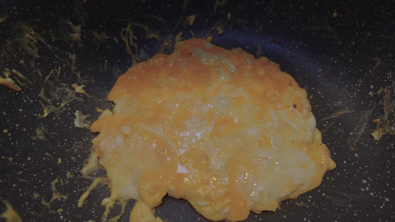 Dolly shot of a whisked egg mixture rustic omelet inside a dark, speckled non stick frying pan