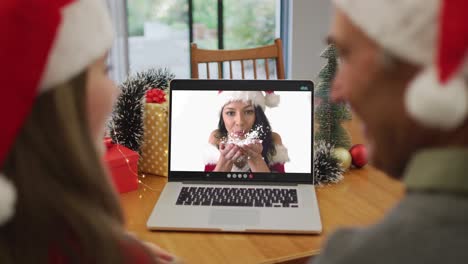 Happy-caucasian-senior-couple-on-video-call-with-female-friend-at-christmas-time