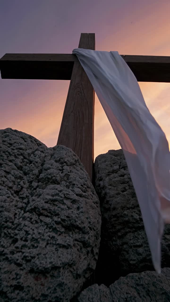 Low-angle video shot of a wooden cross draped with white cloth against a sunset sky