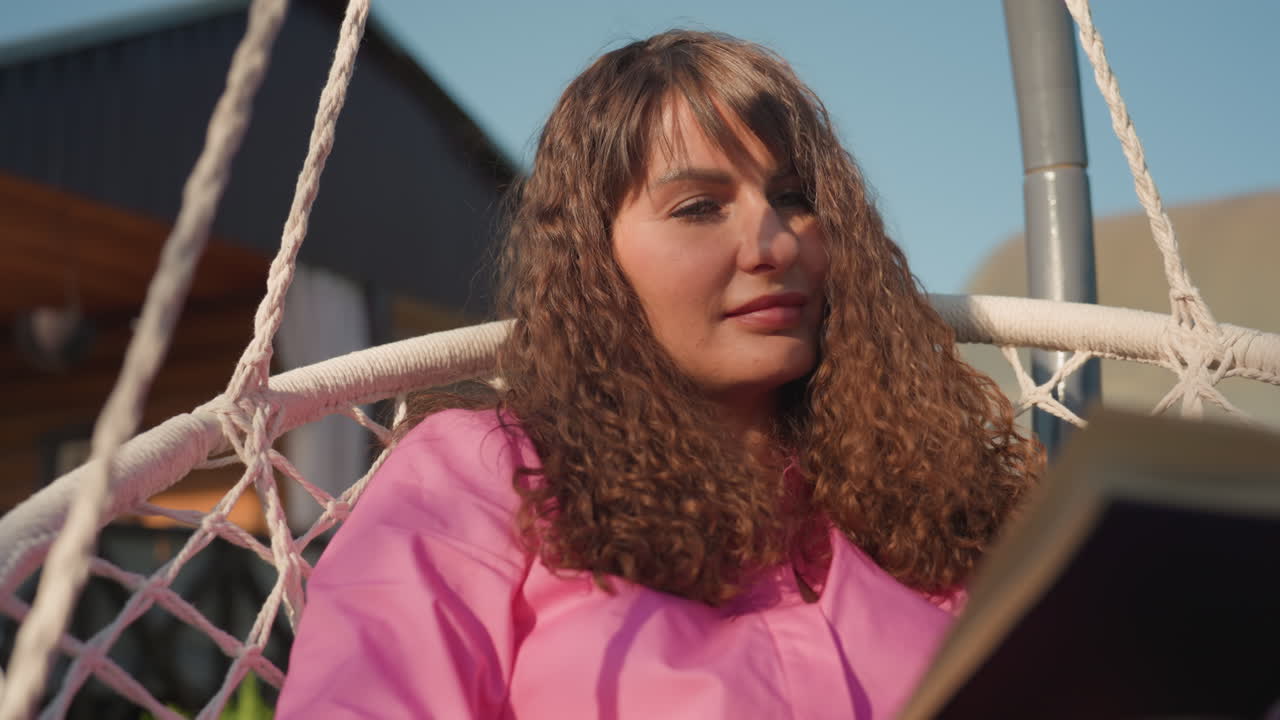 Female Seated On Swing Peacefully Reading At Dusk, Girl On Garden Swing Savoring Tranquil Evening With Book, Woman Peacefully Sitting On Garden Swing Immersed In Her Favorite Book During Sunset