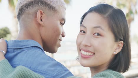 portrait of happy biracial couple embracing on promenade, in slow motion