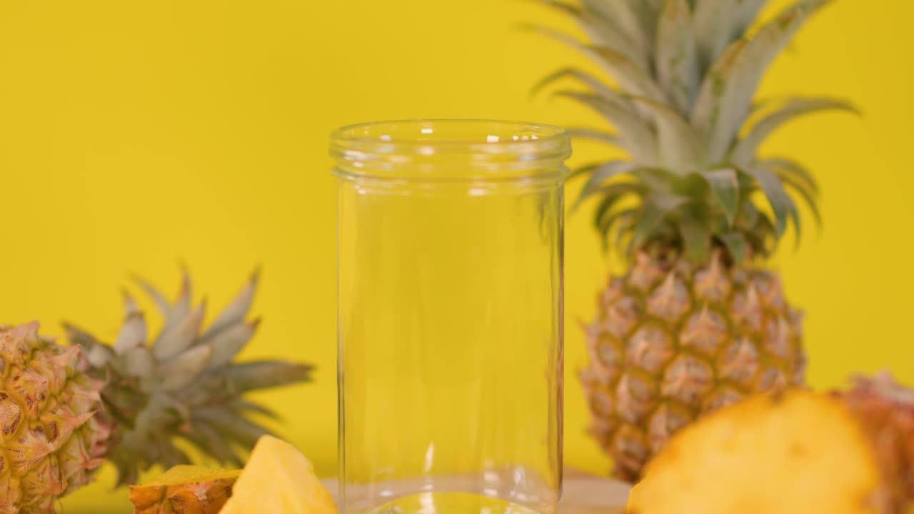 Creamy pineapple smoothie pours into glass, surrounded by fresh fruit, under bright, even lighting