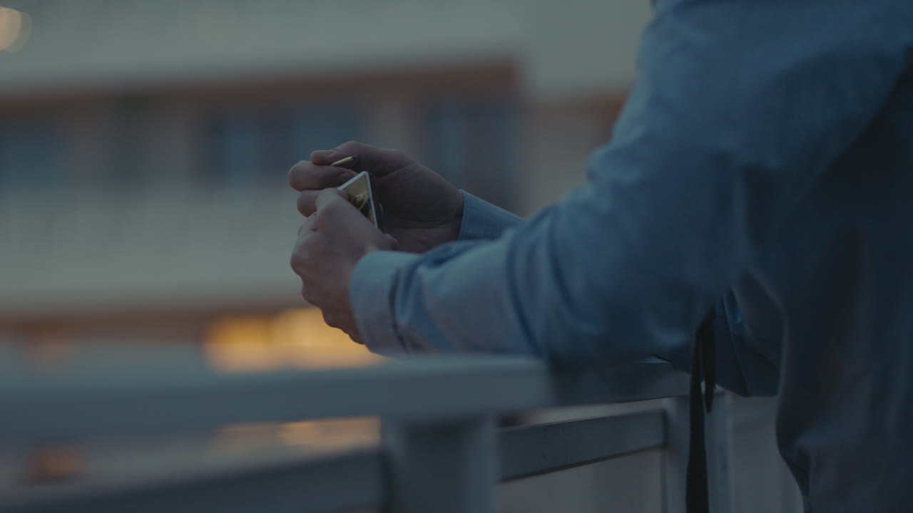 A sad man in a shirt smokes a cigarette on the balcony