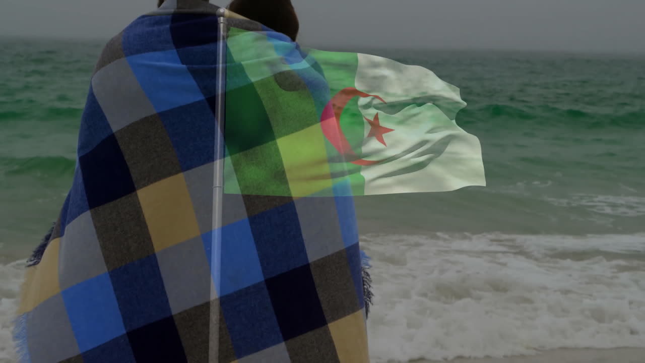 Wrapped in blanket by ocean, couple with Algerian flag animation overlay