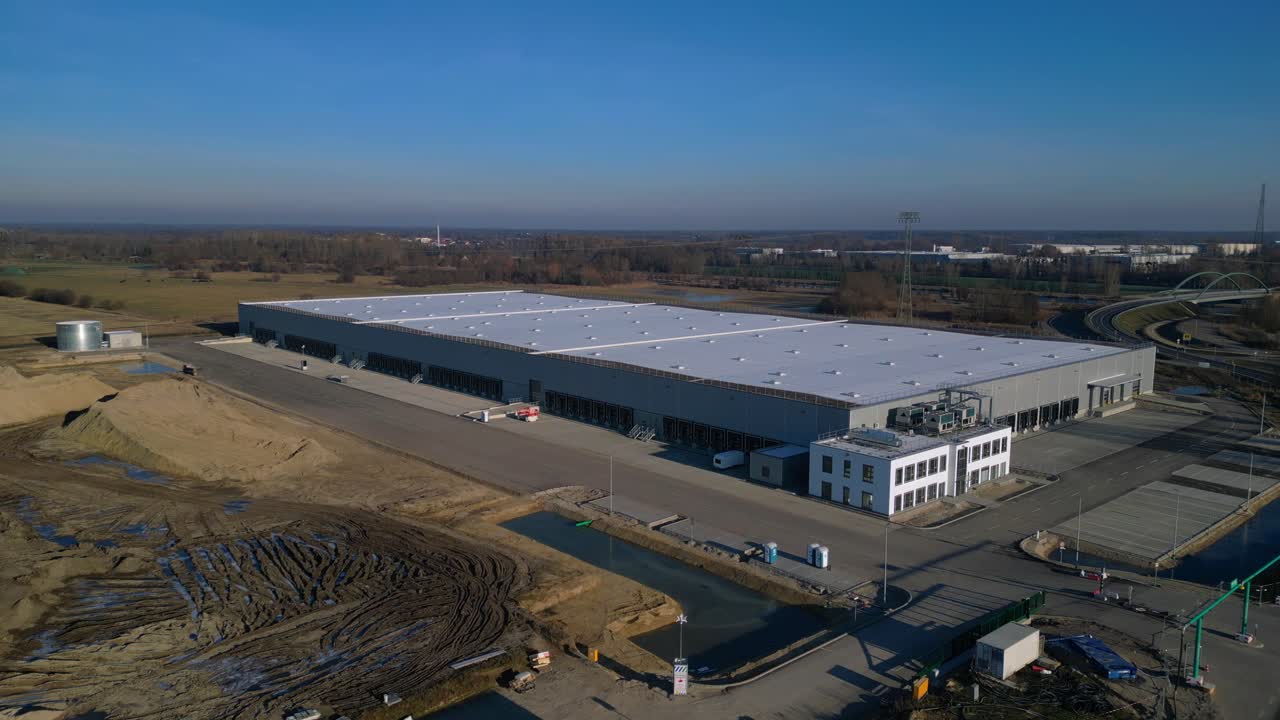 Nuovo grande centro logistico in costruzione con un'ampia area di stoccaggio, banchine di carico e terreno vuoto circostante. Vista aerea spettacolare con drone panoramico statico su treppiede
