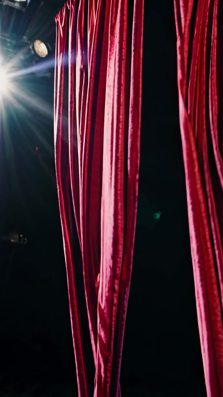 Scena teatrale drammatica con sipario rosso e spotlight da un'angolazione laterale, che evoca un video cinematografico.