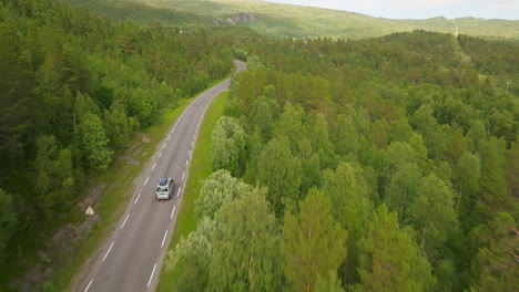 campervan drives along winding mountain road lined with green forest, aerial