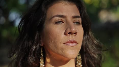 close up of sun hitting face of blue-eyed brunette woman with nose piercing. slomo