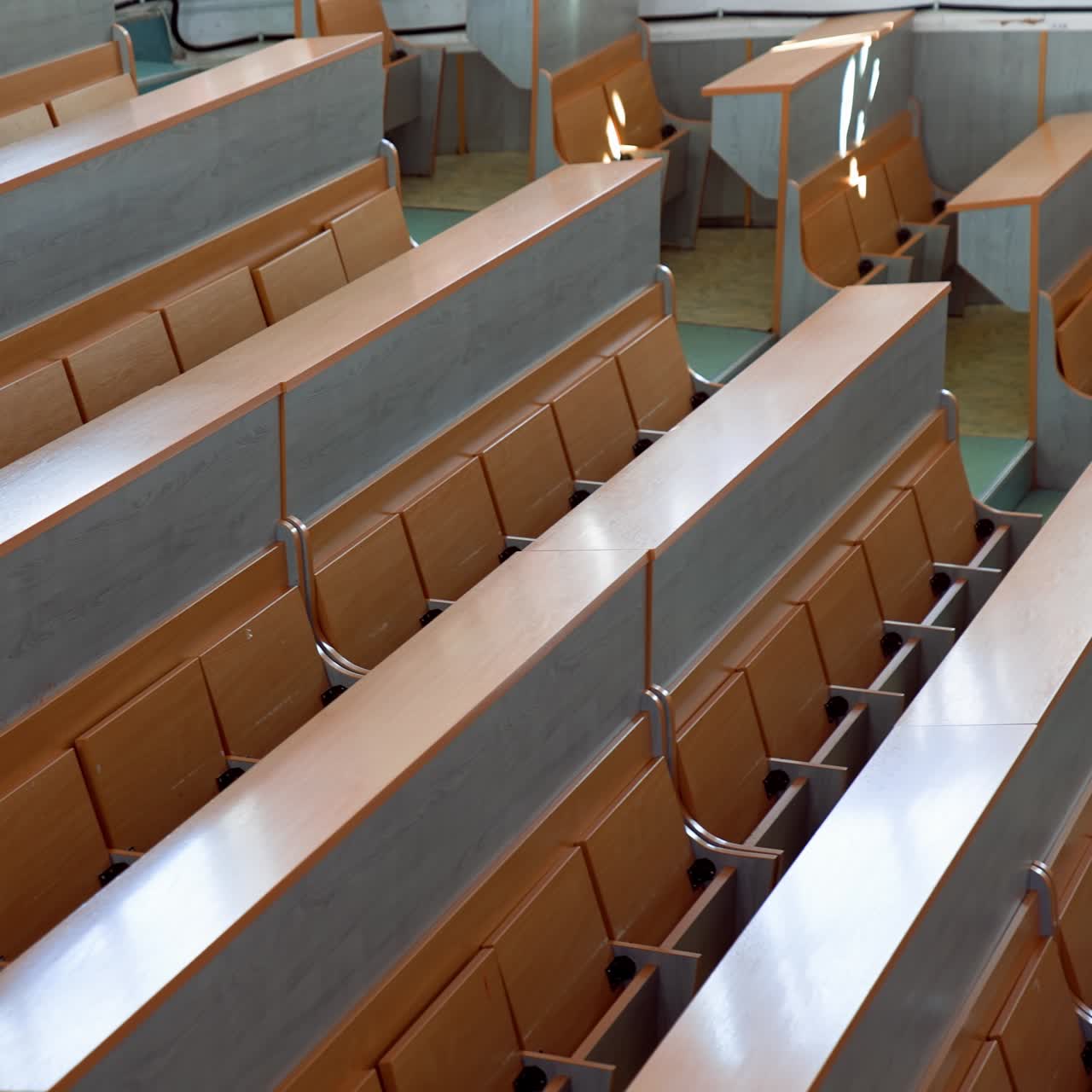 Modern desks in lecture hall. Rows of long wooden tables with vacant seats in the light auditorium at university. Classroom without students