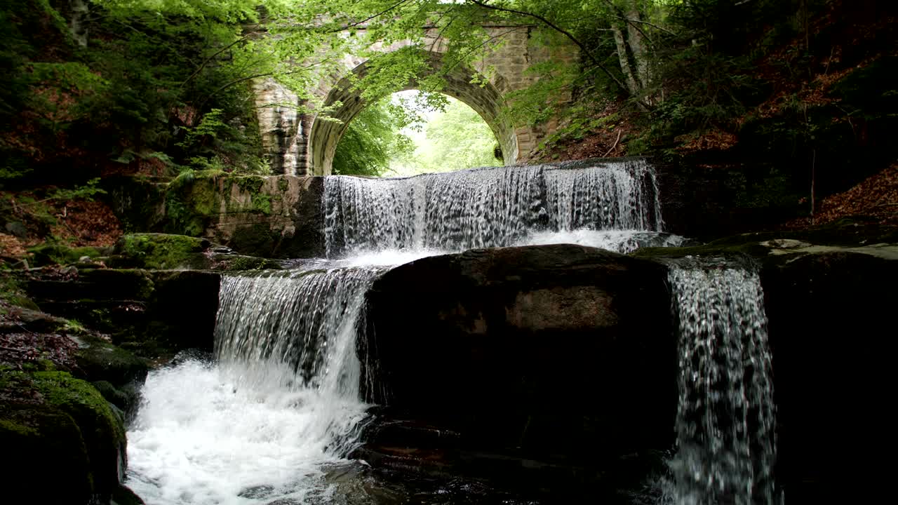 cámara lenta de una cascada épica y un puente romano