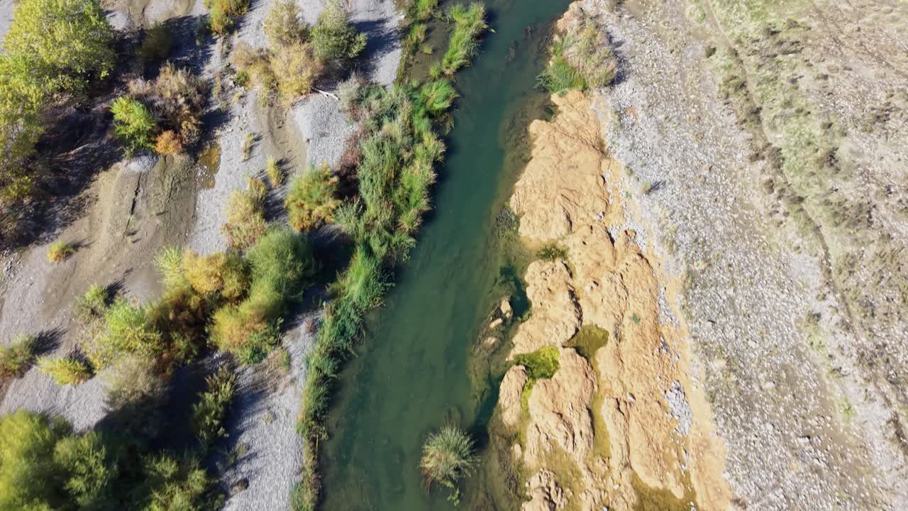Drone flies in a straight top-down view along a shallow section of Cache Creek, showing dry rocky banks and dense vegetation in Capay, California