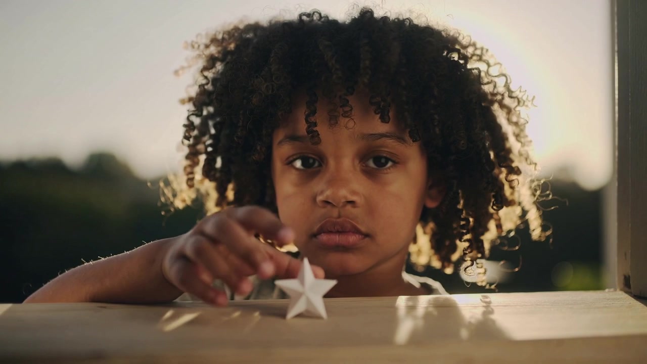 Lifting small white star, child in light short-sleeve shirt placing it upright on porch ledge