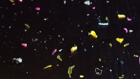 microplastic fragments bounce on a dark table in slow motion, symbolizing overuse and pollution