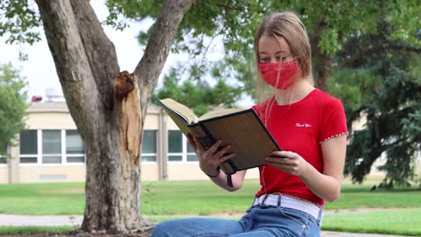 a young student reads while social distancing and wearing a mask on campus