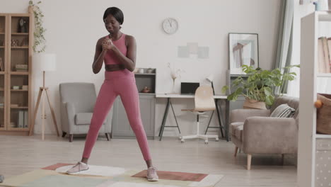 young african-american woman doing squats at home